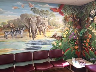 A waiting room with a mural of African animals and lush vegetation, including elephants, zebras, and plants.