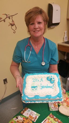 Woman in blue scrubs, stethoscope, holding a cake that says 