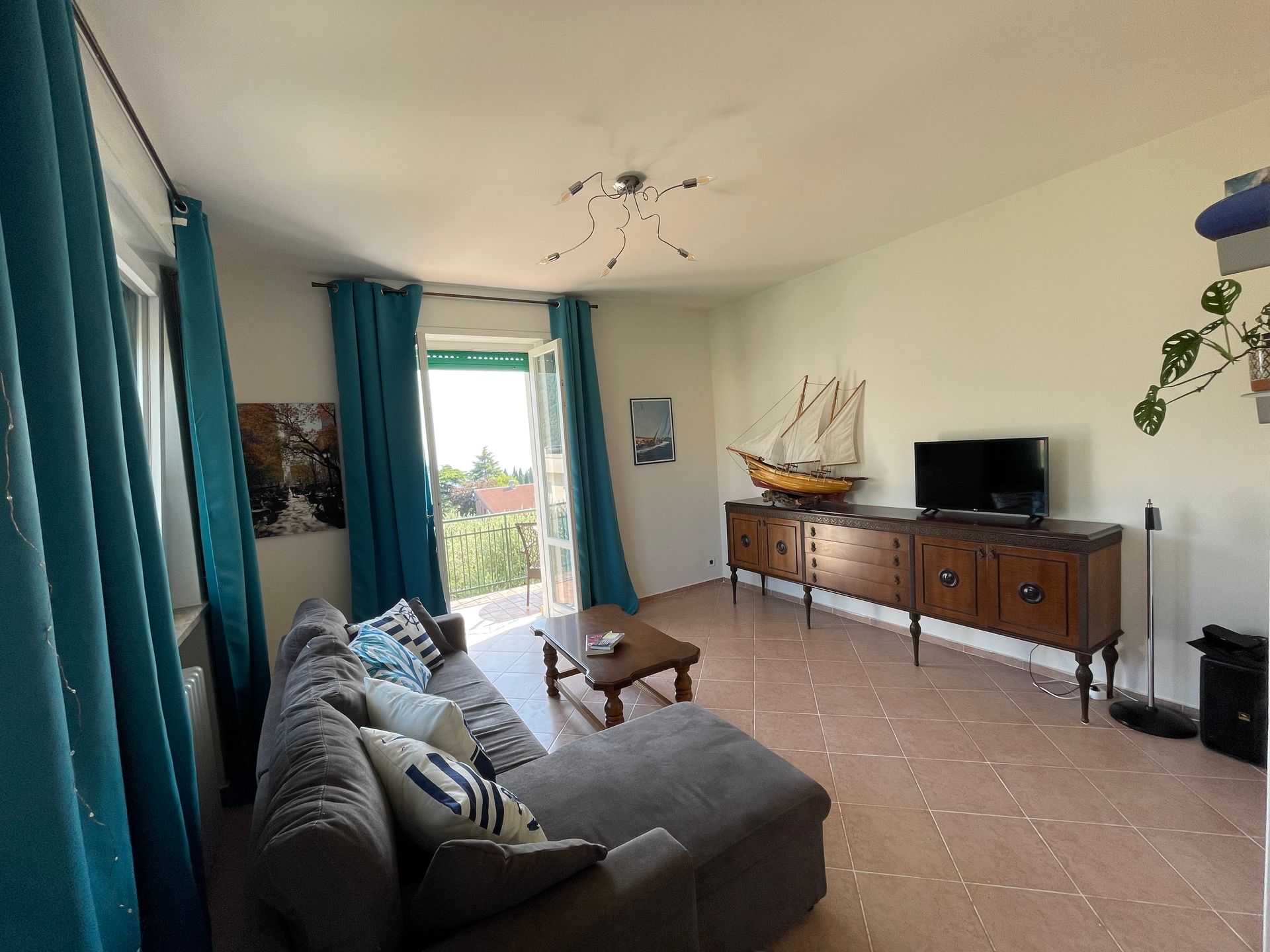 Salotto con ampio divano letto grigio e cuscini marinari, tavolino da caffè in legno e console in legno vintage con smart TV on demand modellino di veliero in legno 