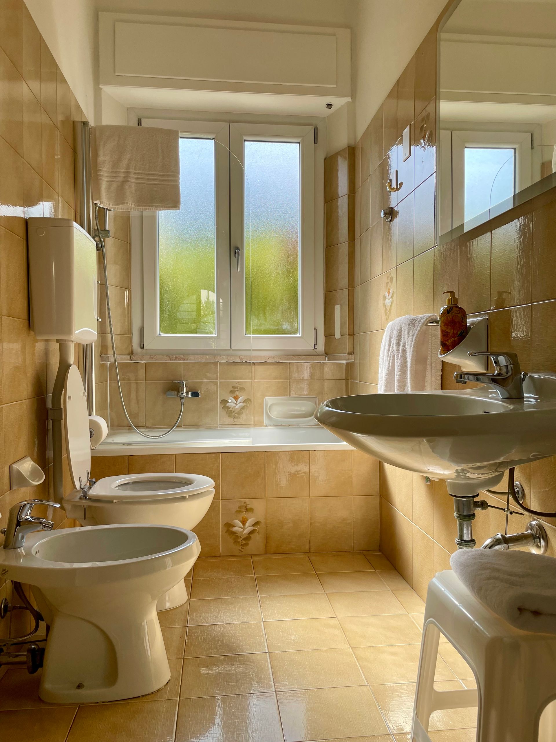Bagno piccolo ma essenziale con vasca da bagno con doccia sotto la finestra da sui non si vede fuori, lavandino con specchio, phon e asciugamani forniti dalla struttura