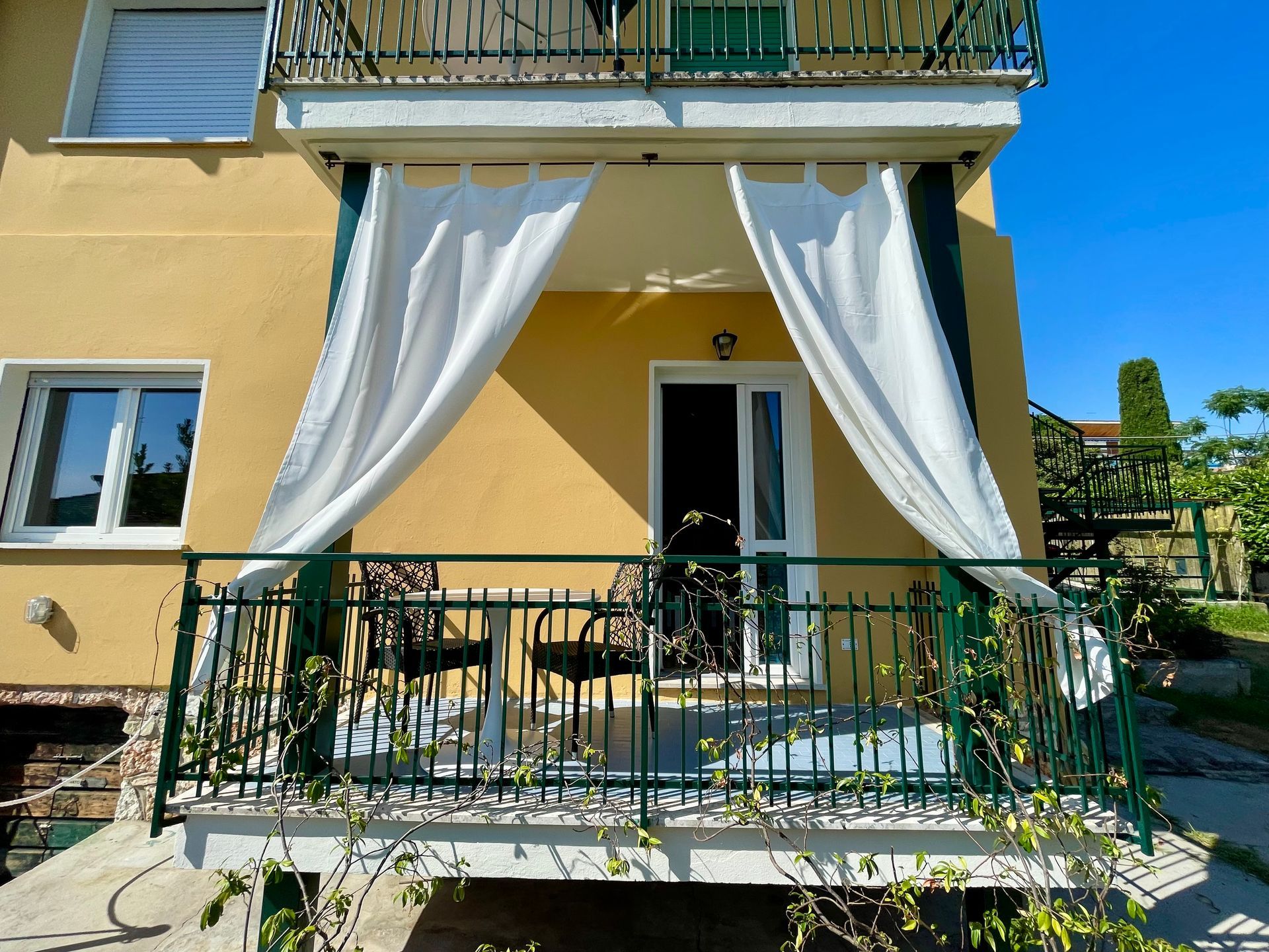 Vista frontale dell'appartamento con in primo piano il balcone coperto con tavolo e sedie e le tende bianche per il sole