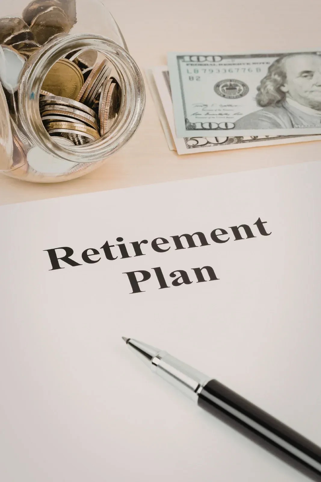 Retirement plan document with pen, jar of coins, and cash on a table.