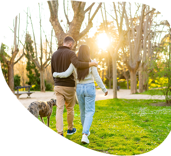 Couple walking arm in arm with a dog in a sunny park at sunset