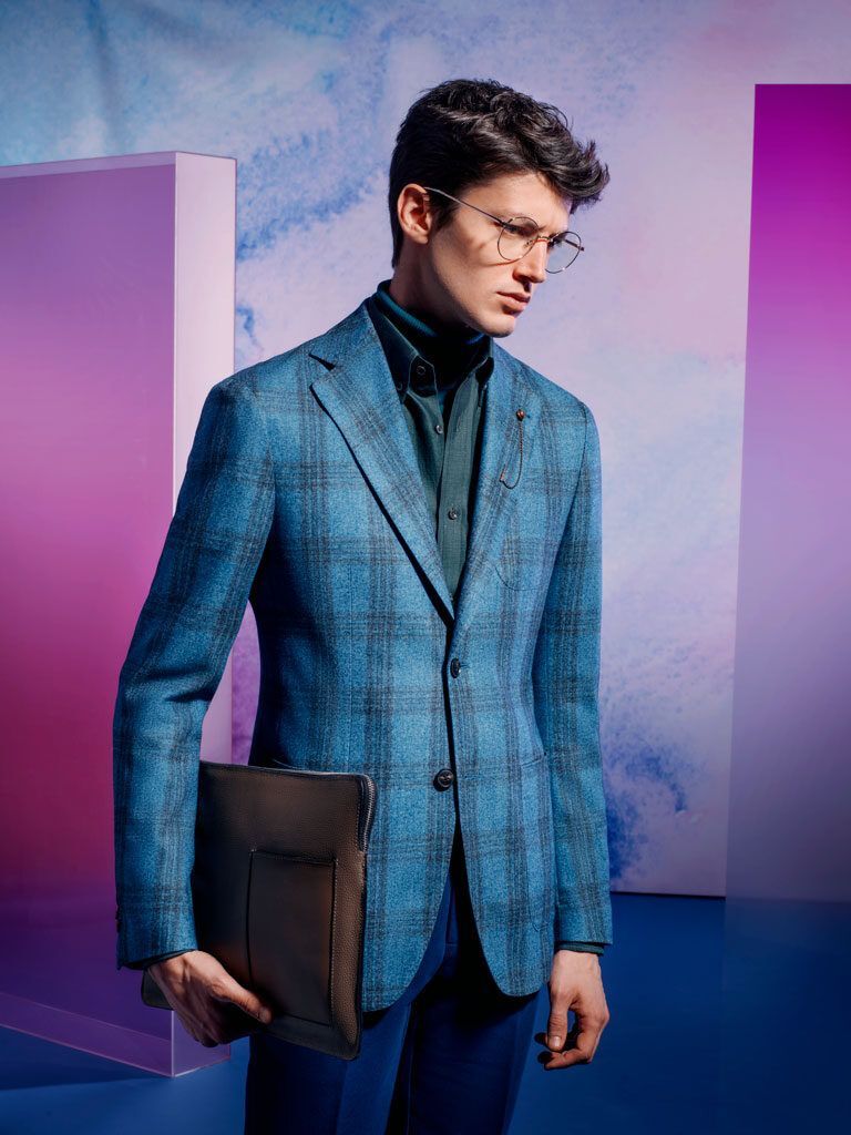 Man in a blue blazer holding a black portfolio against a purple studio backdrop