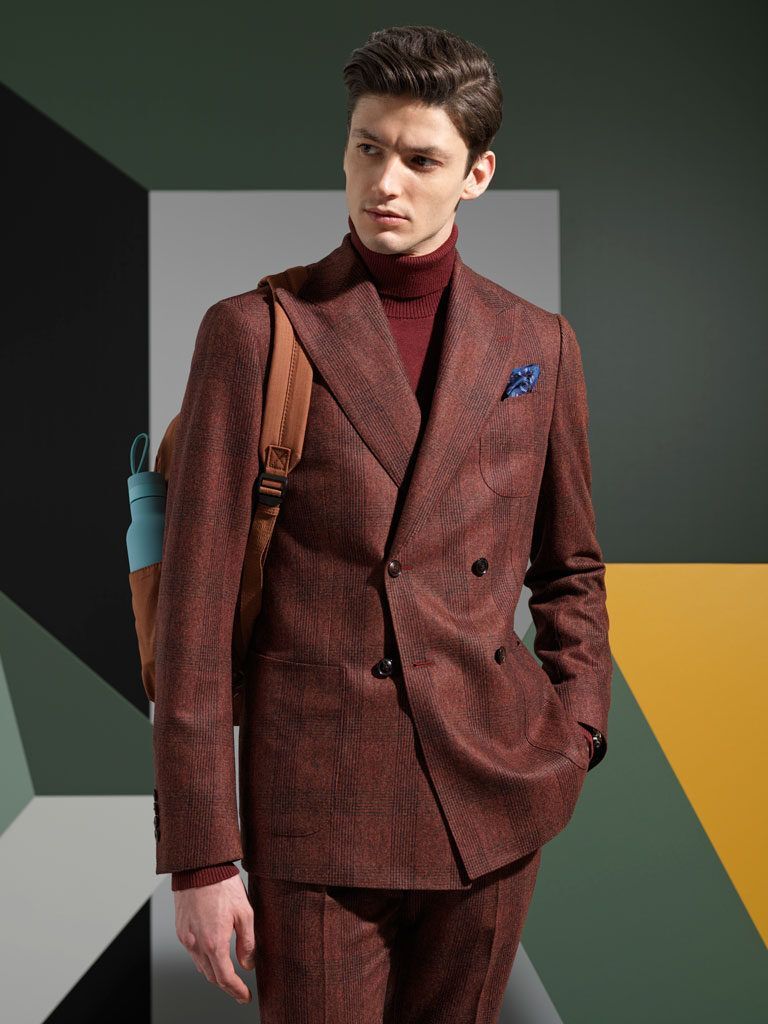 Man in a brown textured suit with a burgundy turtleneck posing against a geometric backdrop.