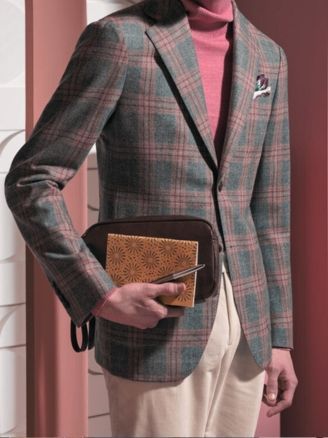 Person in a plaid blazer holding a brown leather clutch against a pink background