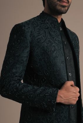 Man in a dark patterned jacket over a black shirt, posing against a neutral background.