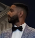 Man in a patterned suit and black bow tie, shown in profile against a dark background.