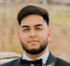 Portrait of a man in a black suit and bow tie, outdoors with a blurred background