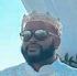 Man wearing sunglasses and a jeweled crown against a blue sky