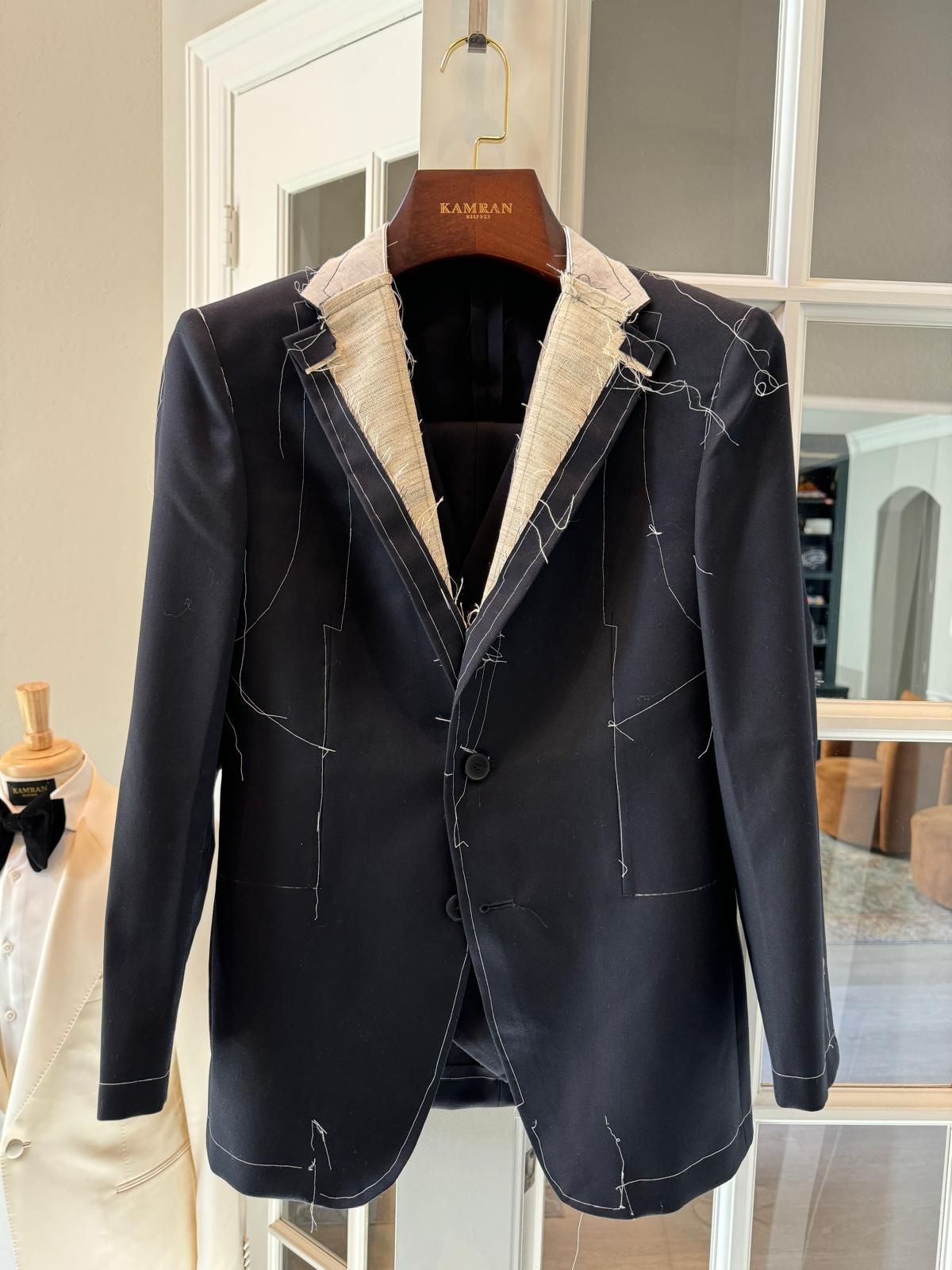 Navy blazer with white flecks hanging on a wooden hanger in a bright room