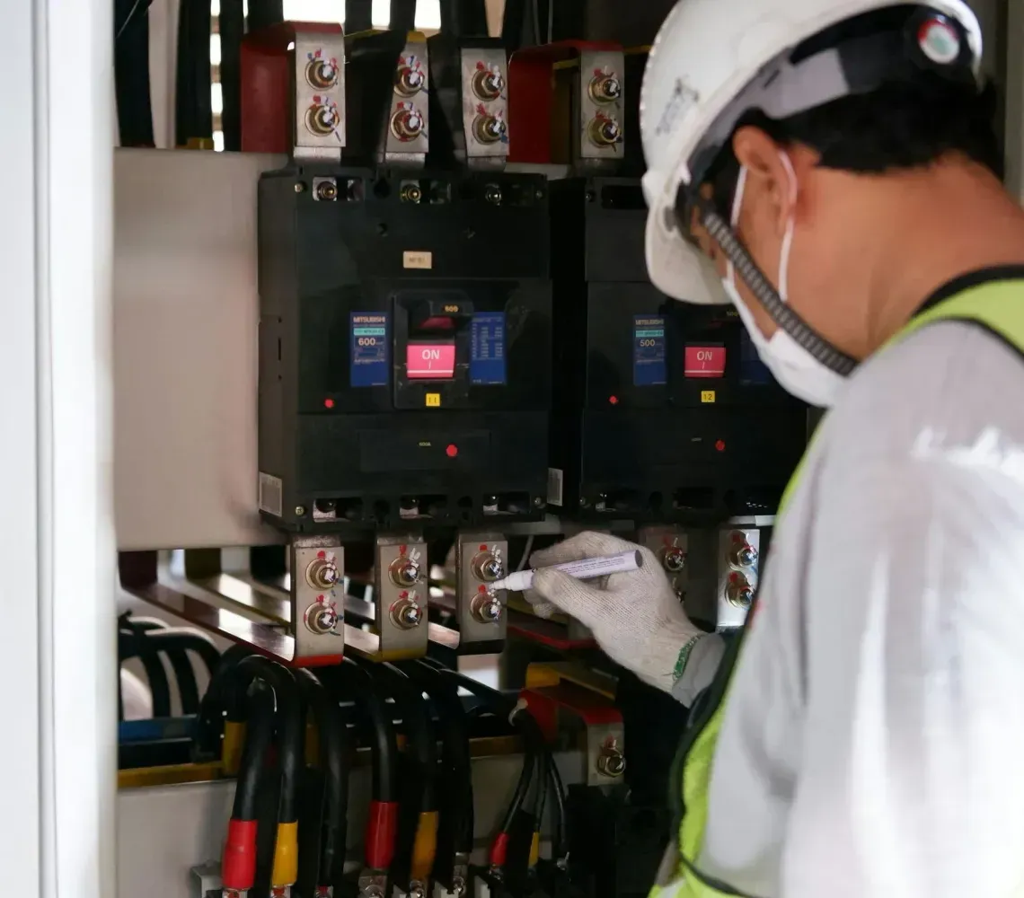 Technician inspecting electrical control panel with wired components and warning labels in an industrial setting
