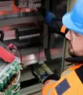 Technician in blue hard hat inspecting electrical control panel with wiring inside a cabinet
