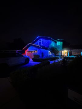 House outlined in blue and red holiday lights at night, with a lit driveway and dark yard.