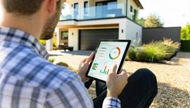 Person using a tablet outside a modern house with charts on the screen