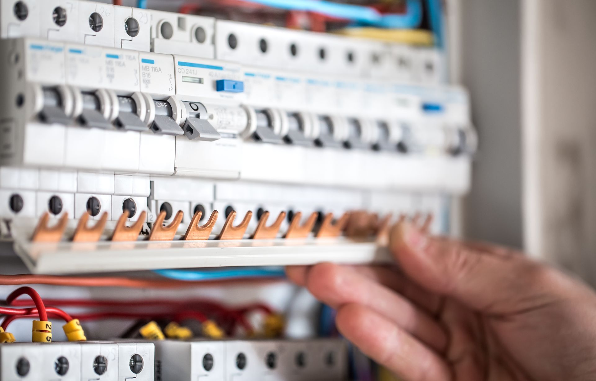 Hand adjusting a row of orange electrical switches in a circuit breaker panel
