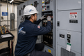 Technician in hard hat adjusting controls inside an industrial electrical panel room