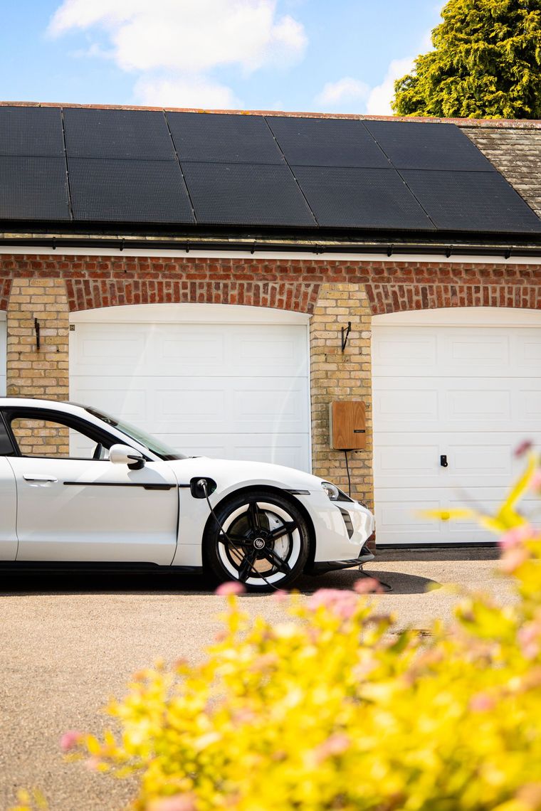 White sports car parked in front of brick garages with white doors, framed by yellow flowers.