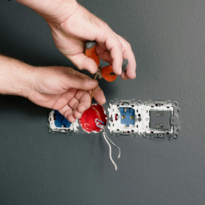 Hands wiring a wall outlet with exposed red and blue electrical wires