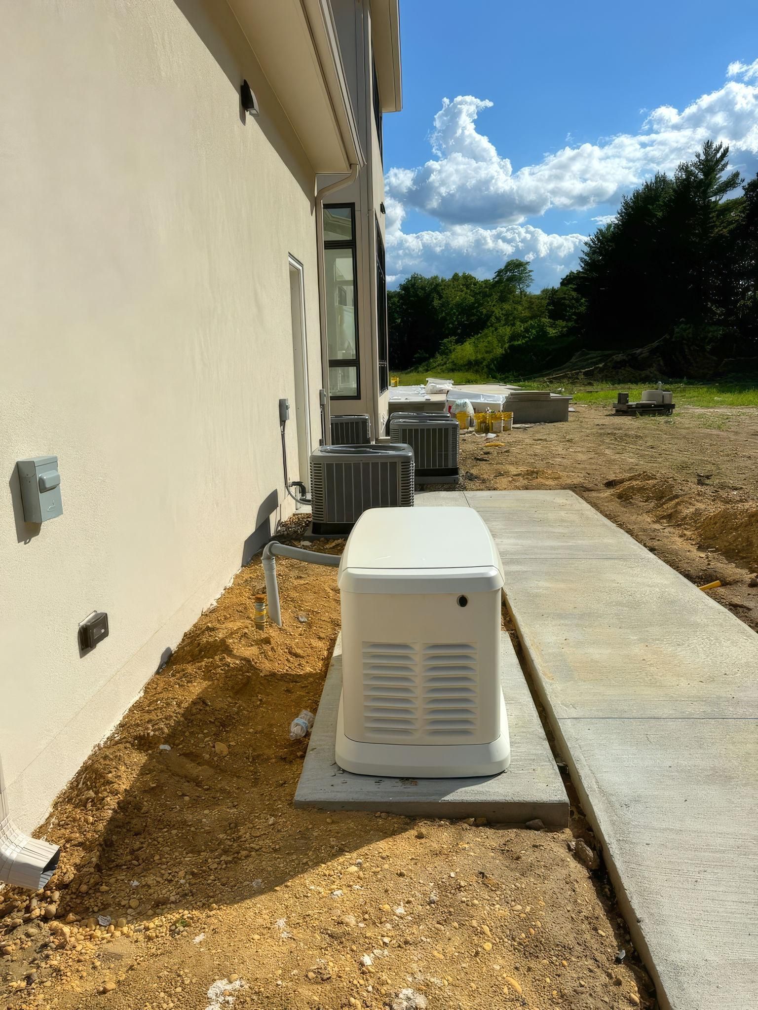 White outdoor AC unit beside a beige house wall on a concrete pad, with gravel yard and blue sky.