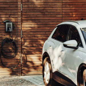 White SUV parked by a wood wall with a wall-mounted EV charger and coiled cable