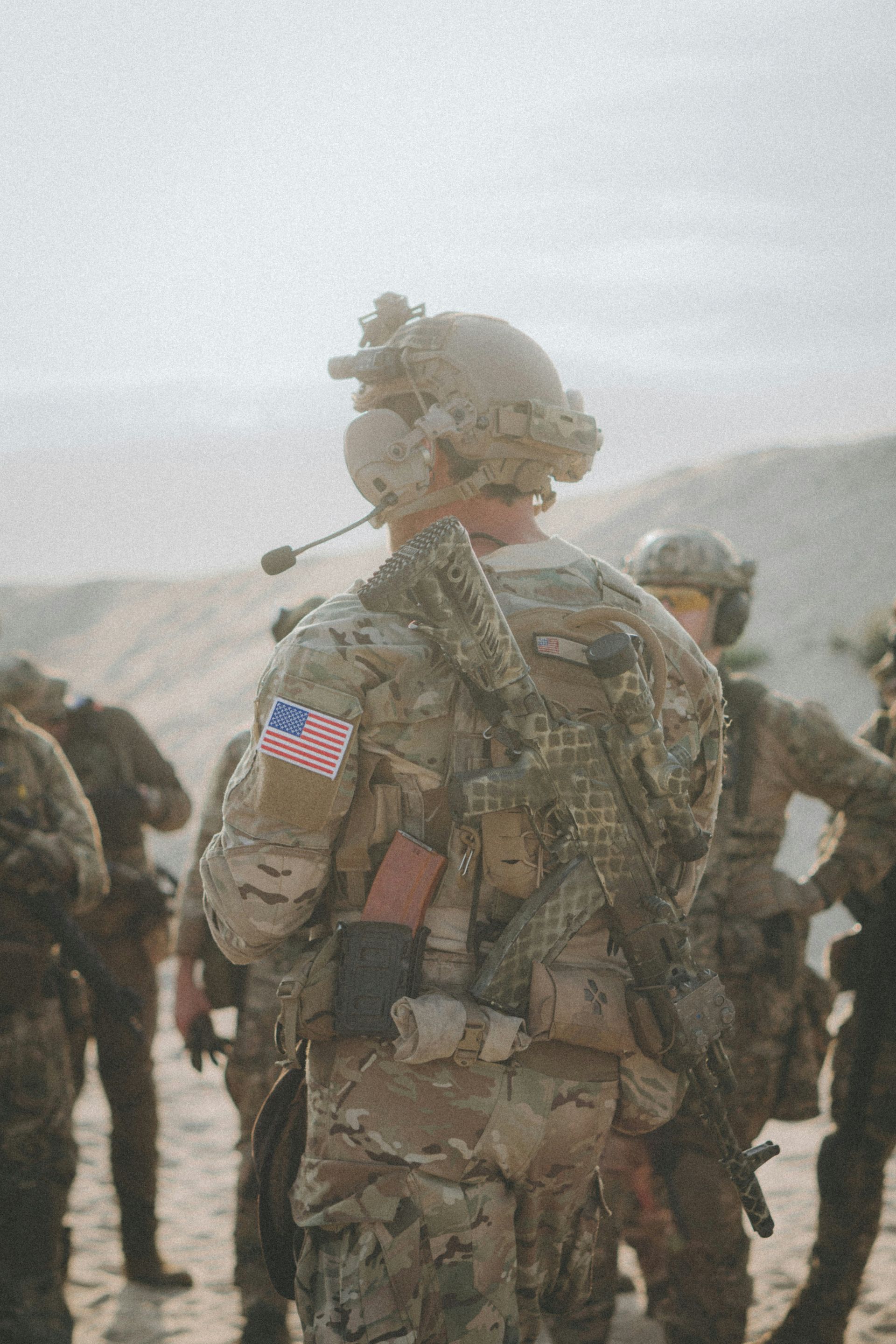 A soldier is standing in front of a large screen with an american flag in the background.