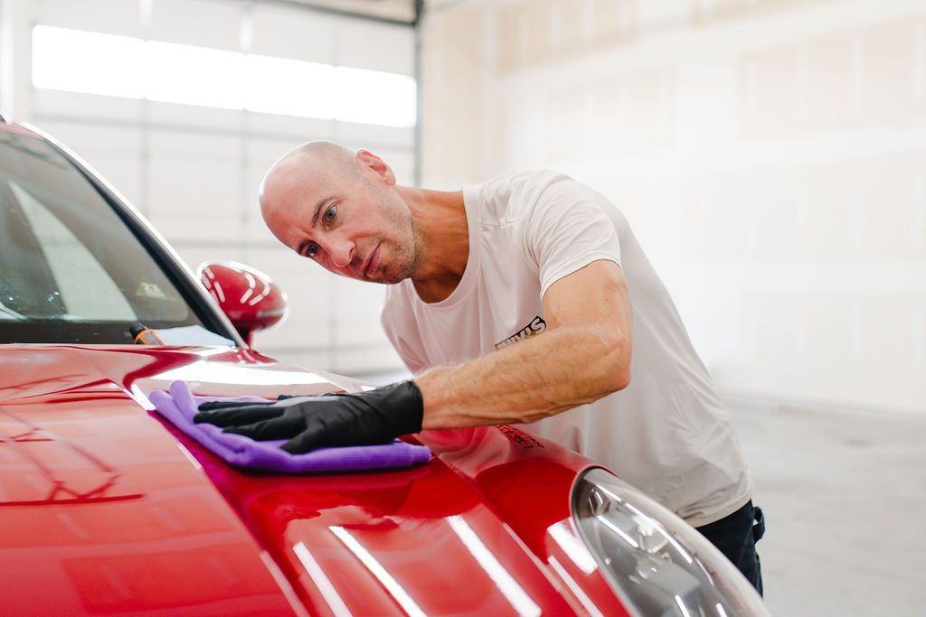 Gloved hand polishing a black car’s hood in a glossy auto detailing shop