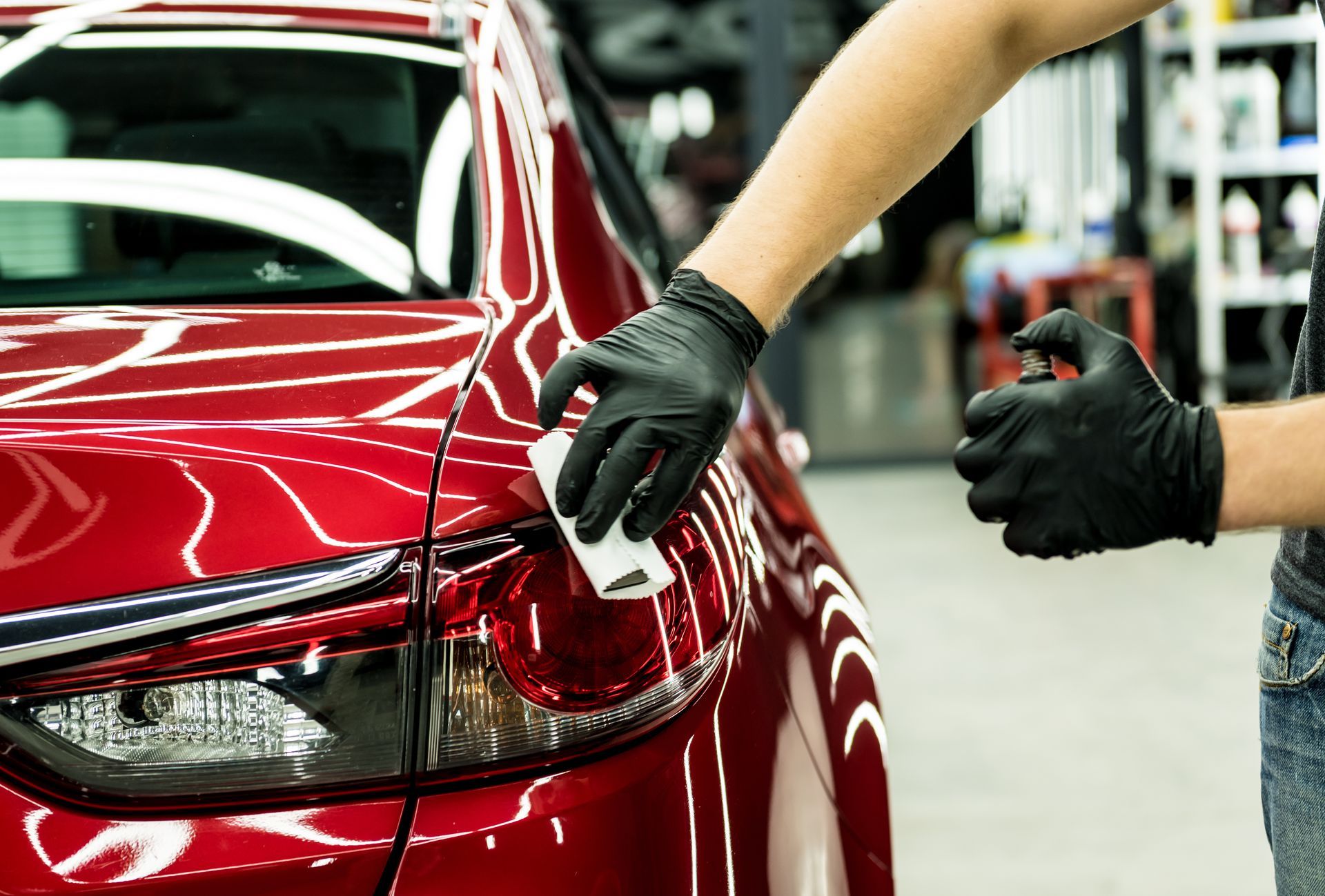 Gloved hands polishing the rear of a red car in an auto body shop