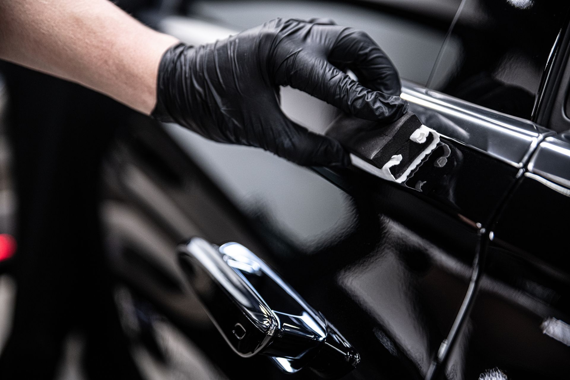 Gloved hand cleaning a black car door with a cloth, close-up