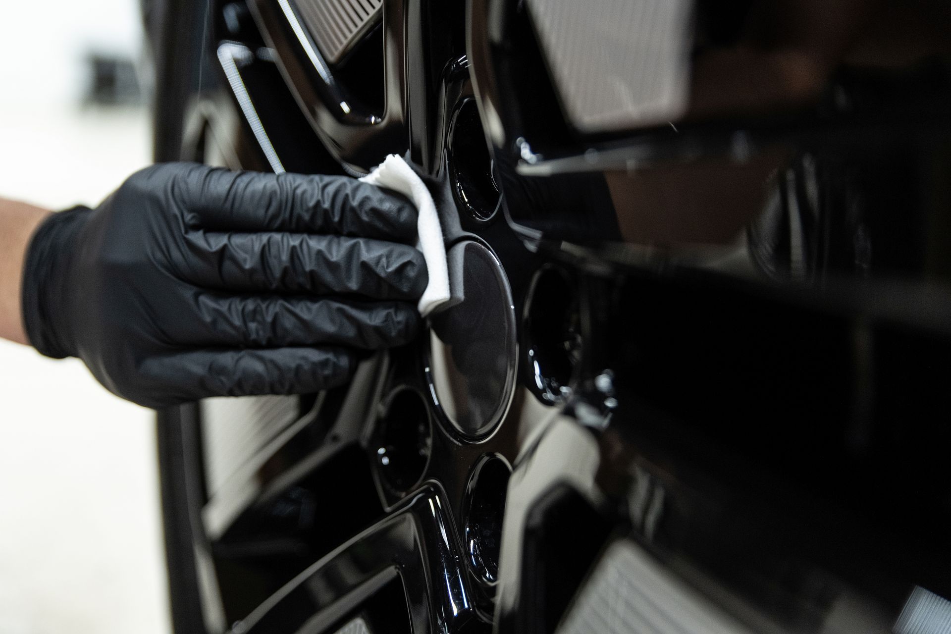Gloved hand polishing a black car wheel with a cloth
