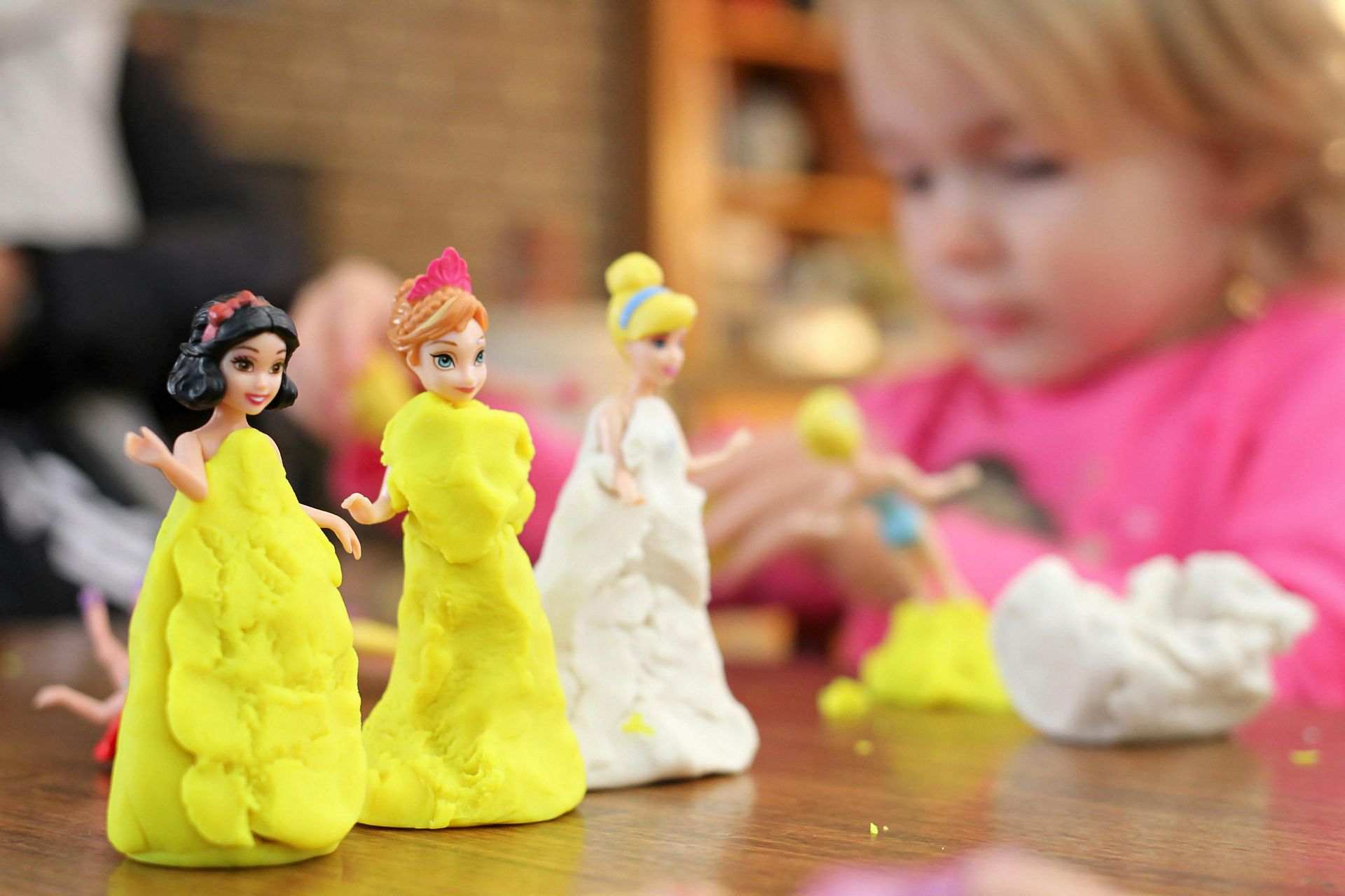 Child playing with Disney princess dolls, covered in yellow and white play dough.