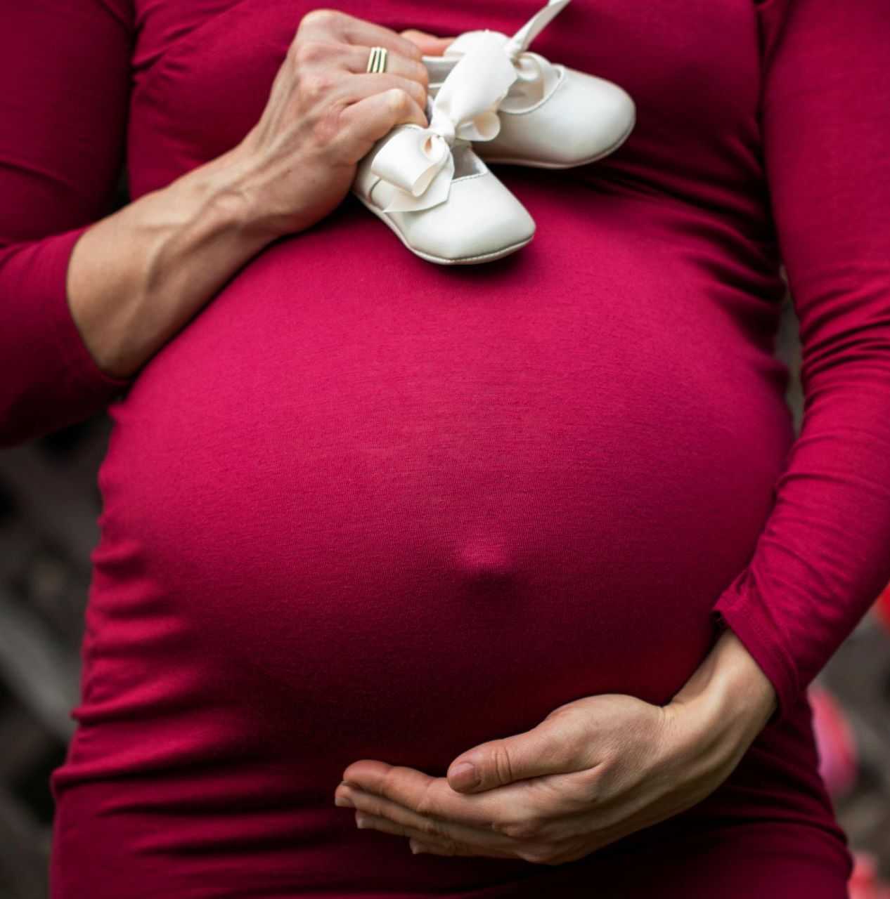Pregnant woman in red dress holding baby shoes.
