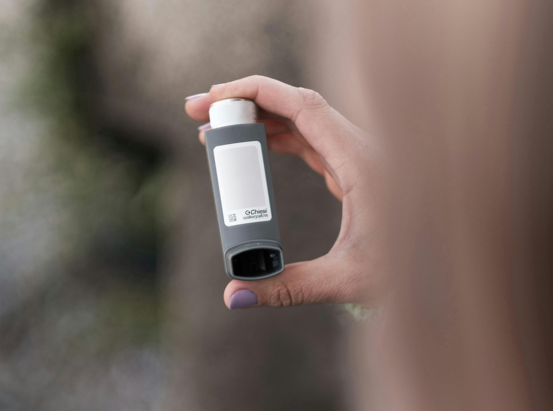 A hand holding a grey and white asthma inhaler.
