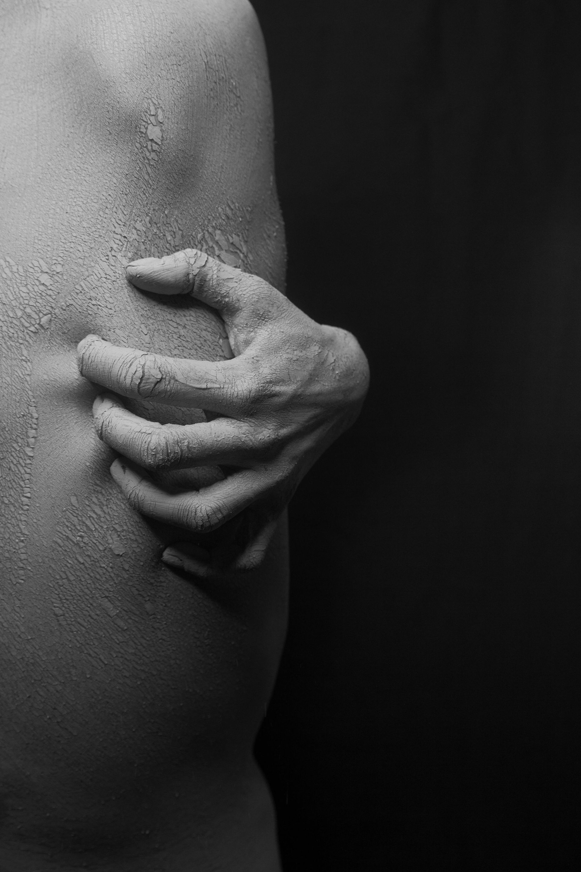 A person's side with a hand clenching the torso, both covered in a textured white substance, dark background.
