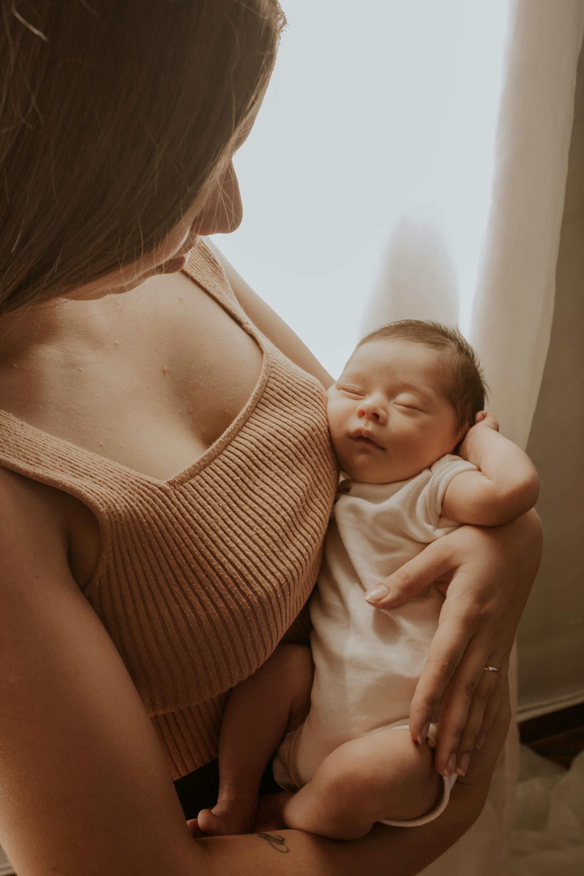 Woman holding a sleeping newborn, lit by soft window light.