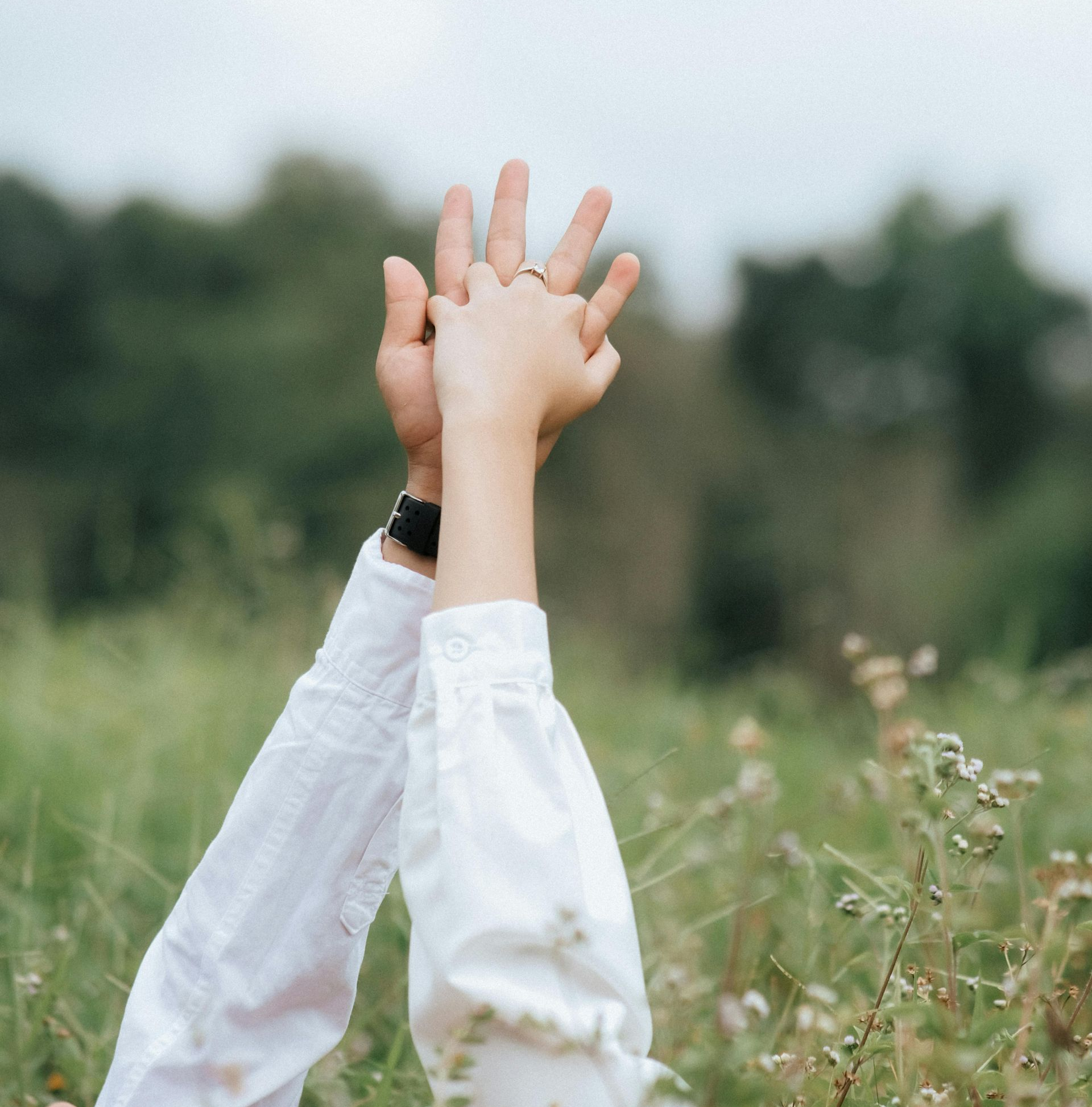 Adult and child's hands high-fiving, white shirts, outdoors in grassy field.