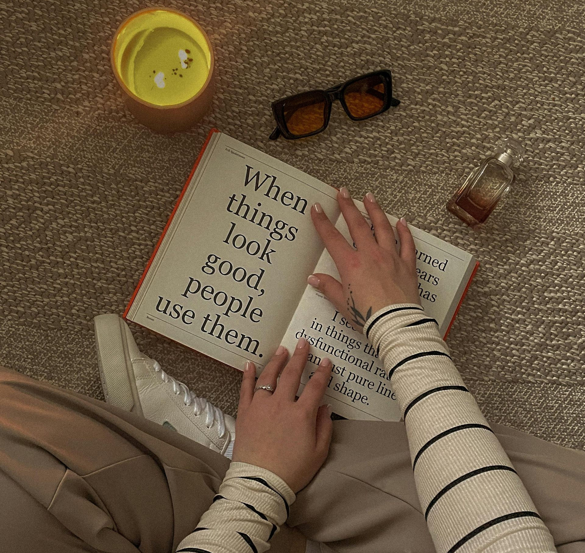 Person reading a book with a quote, surrounded by a candle, glasses, and perfume.