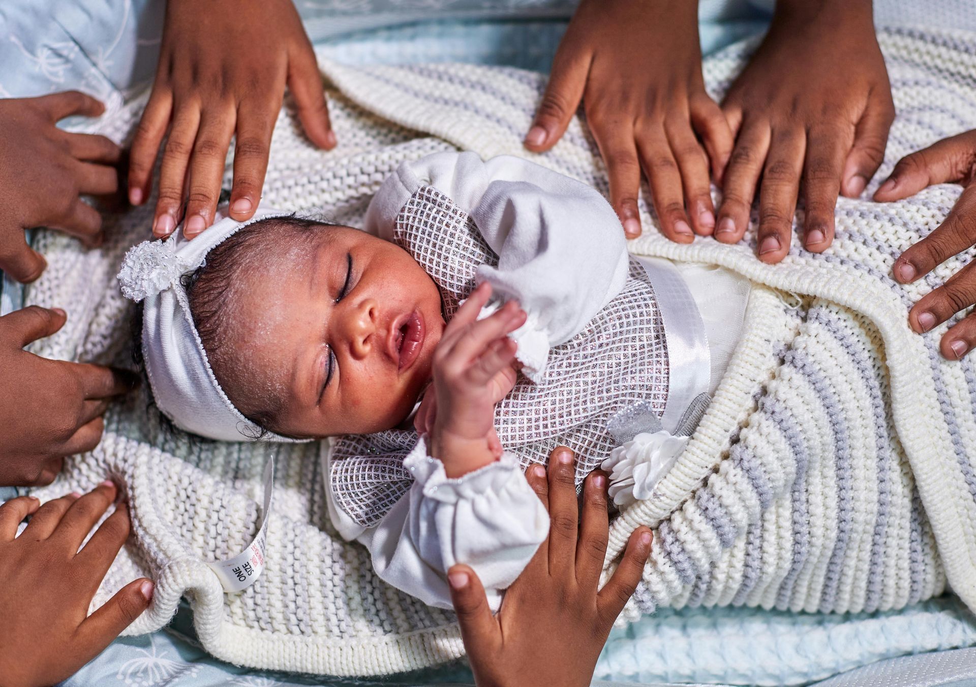 Newborn baby wrapped in blanket, surrounded by several hands.