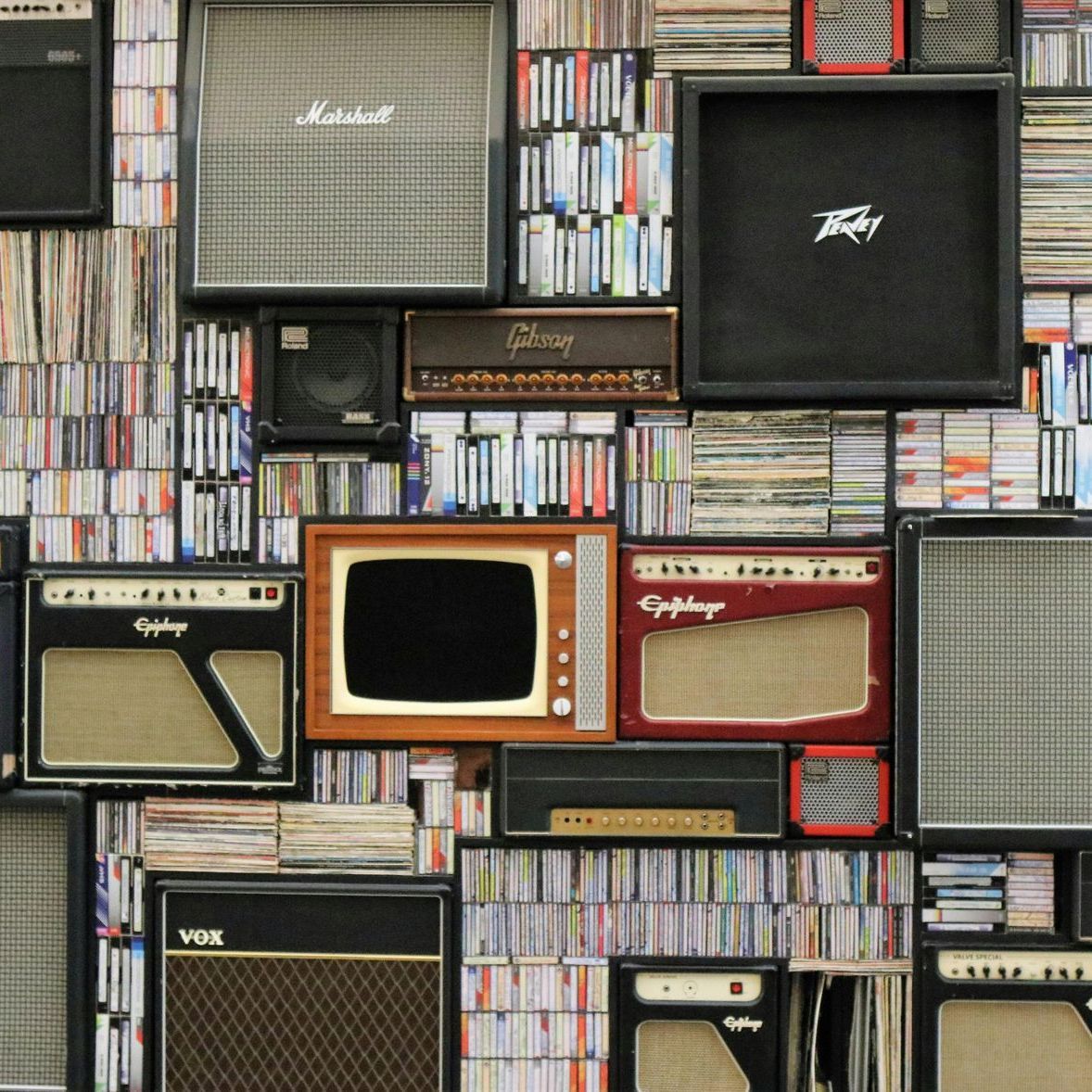 Wall of vintage guitar amplifiers, a retro TV, and stacks of CDs and records.
