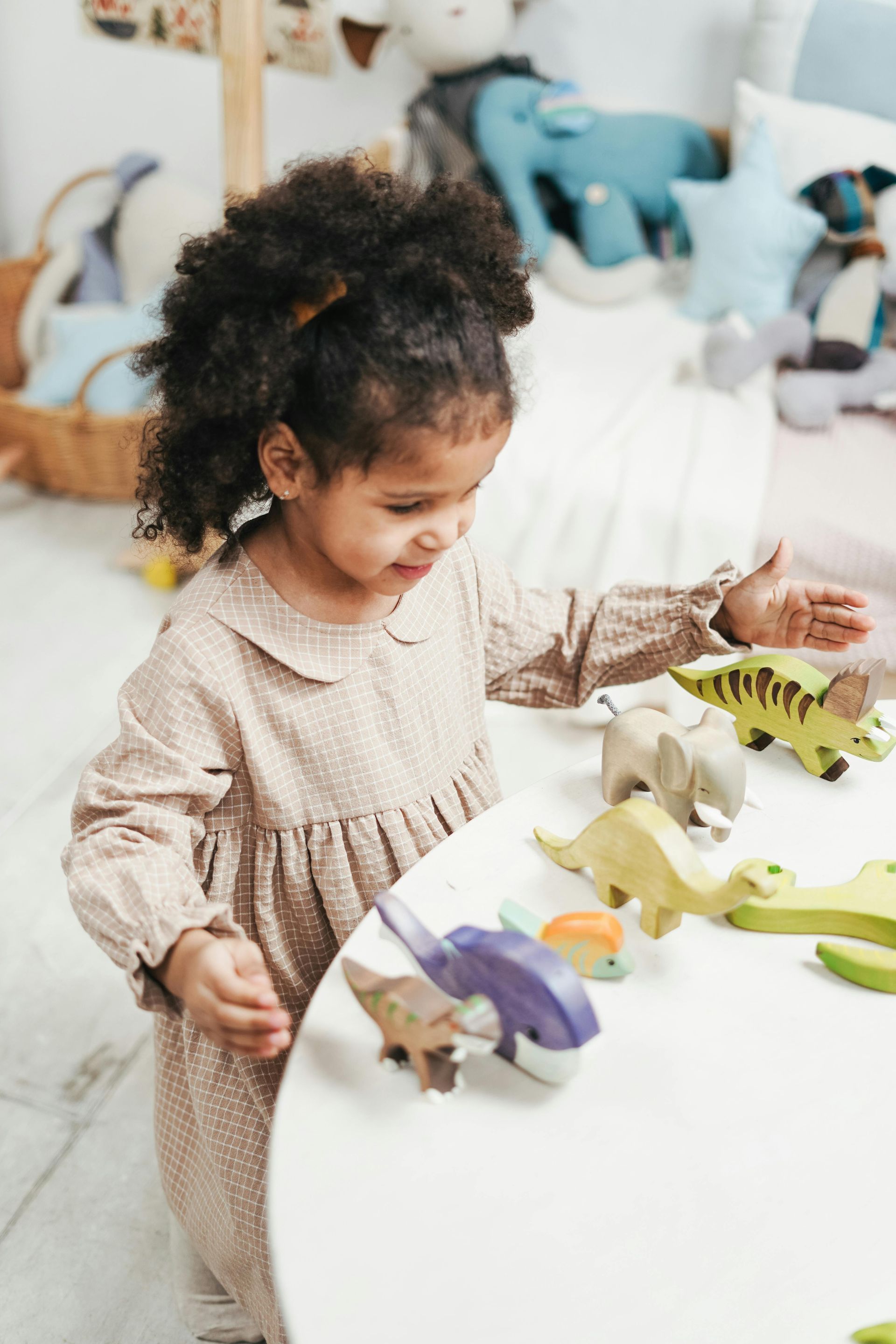 Two young children playing with wooden dinosaur toys and trees on a light wood floor in a bedroom.