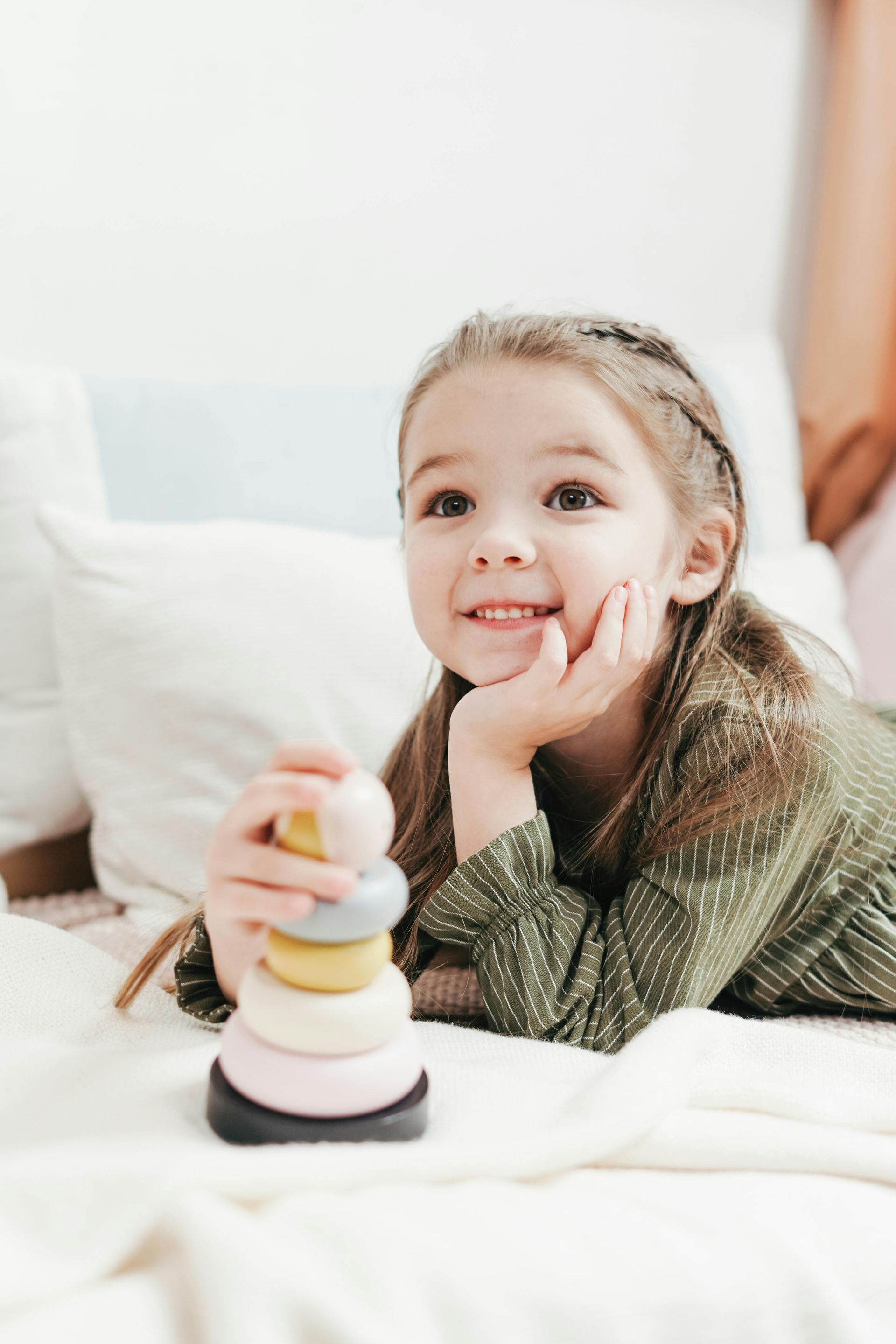 Girl smiles while playing with a stacking toy on a bed.