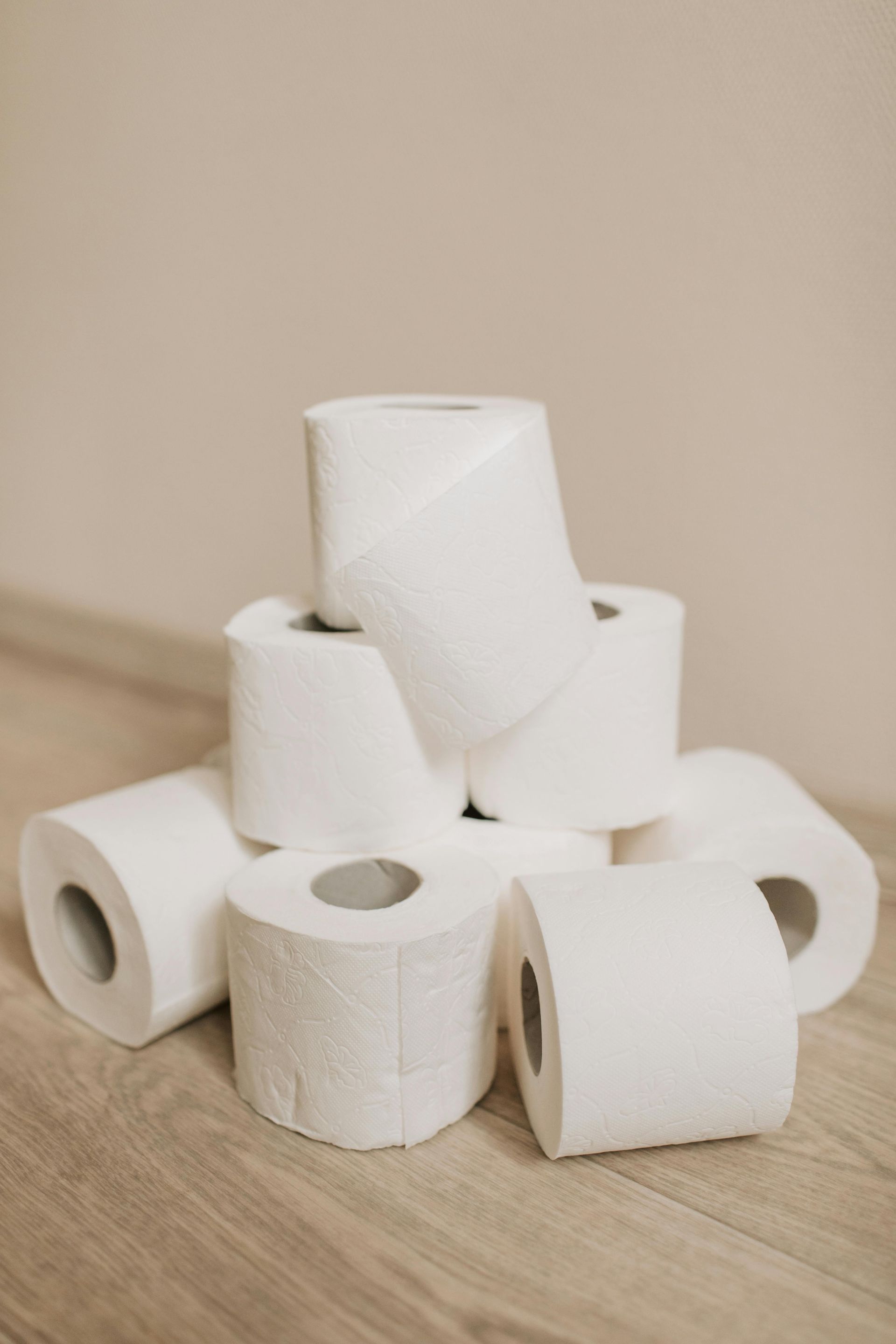 Pile of white toilet paper rolls on a wood floor against a neutral wall.