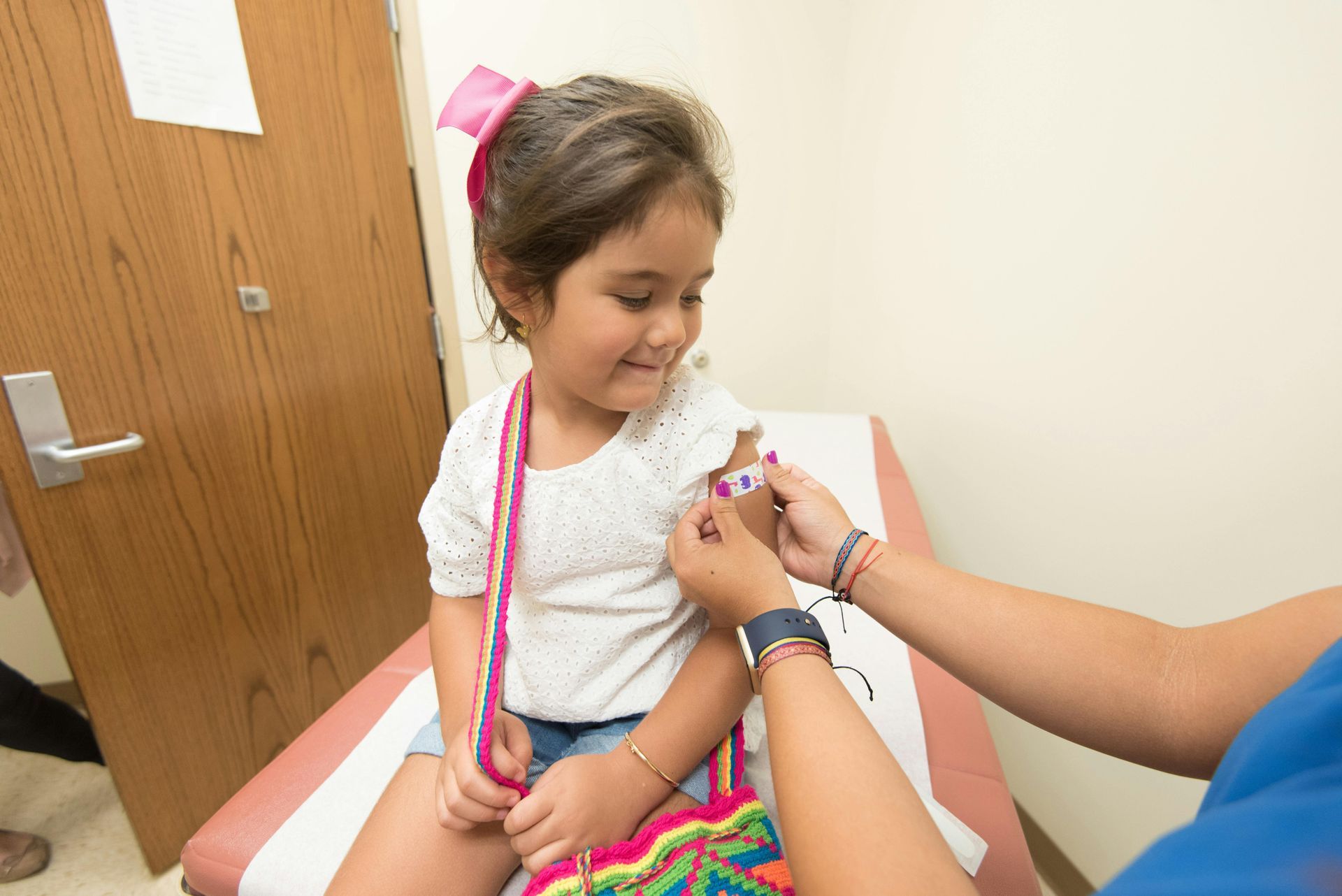 Young girl smiles as a healthcare worker applies a bandage after a vaccination in a doctor's office.
