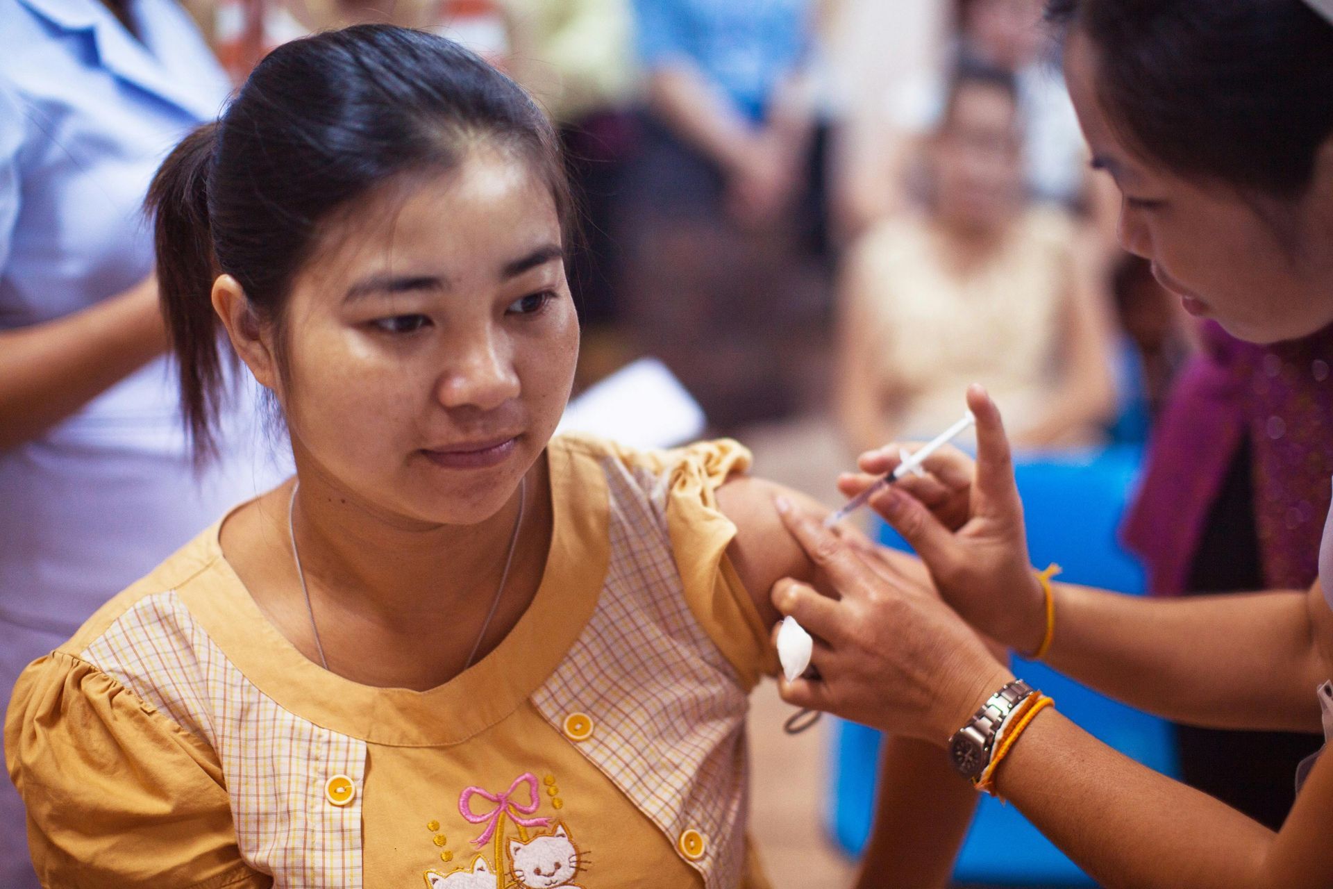 Woman receiving injection in her arm by a healthcare worker in a clinic setting.