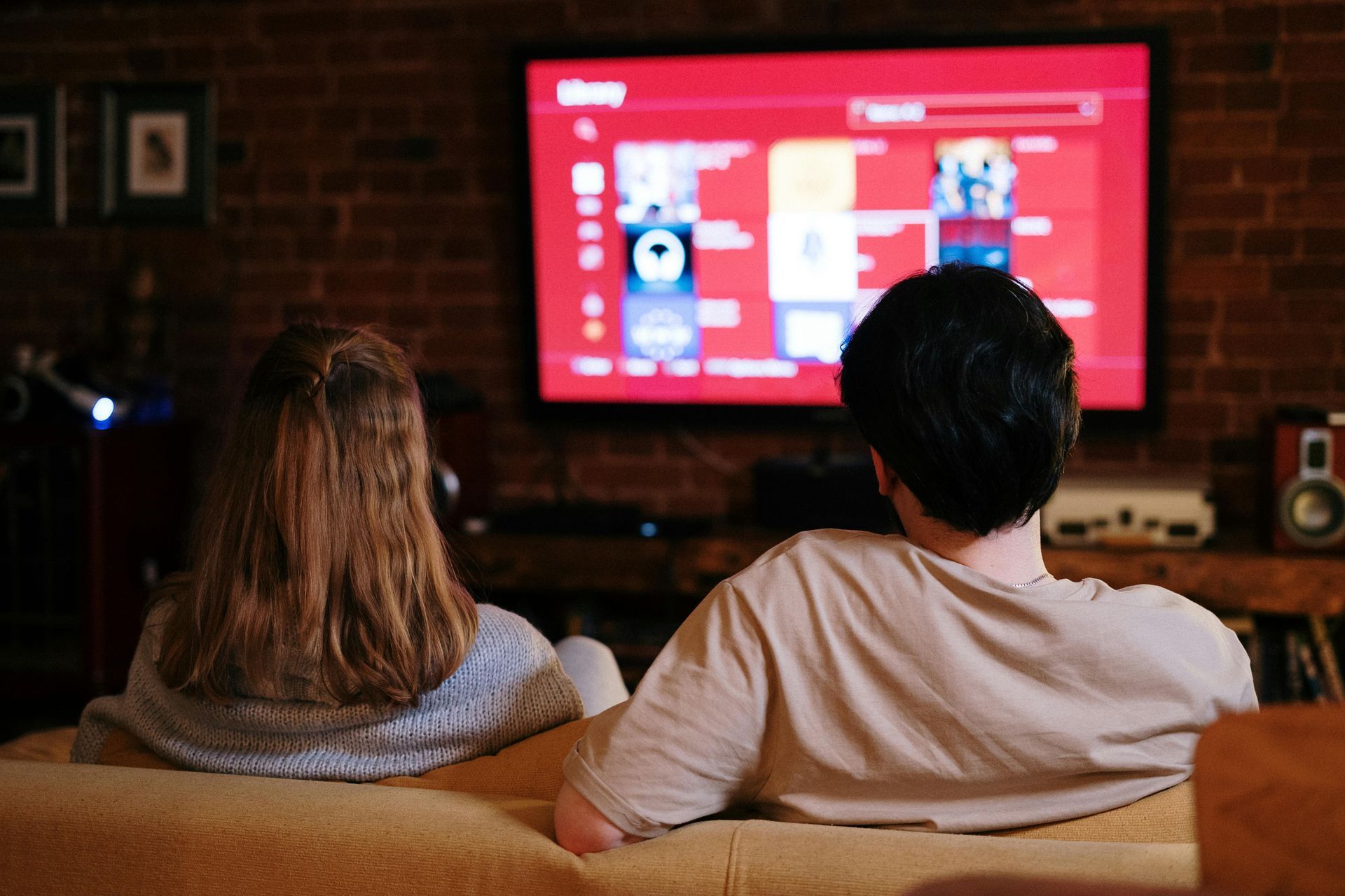 Couple on a sofa watching a large TV screen with streaming app interface, in a dimly lit room.