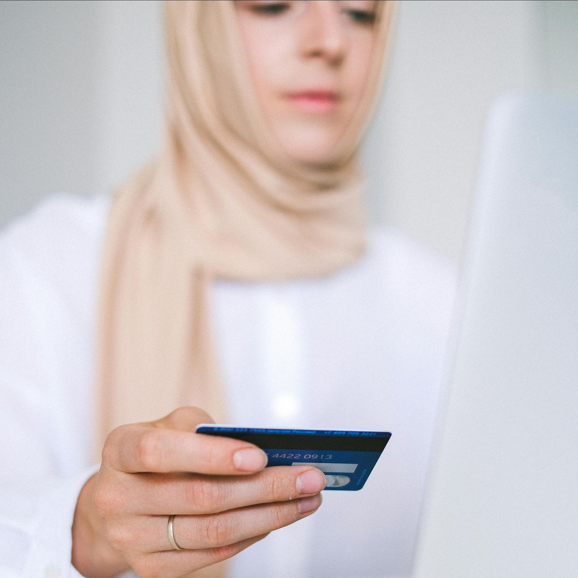 Woman wearing a hijab, holding a credit card, looking at a laptop screen.