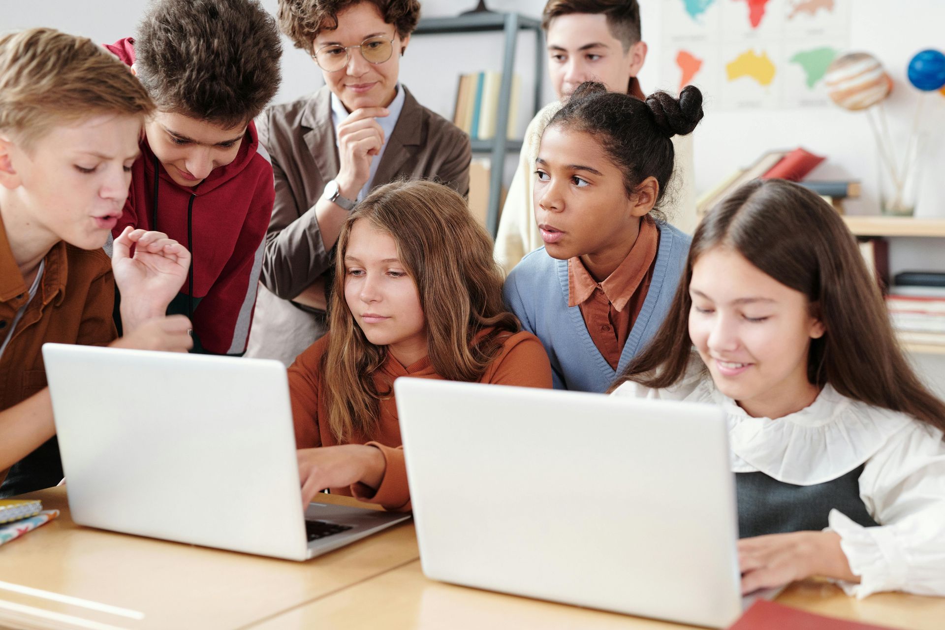 Students and teacher around laptops in a classroom; all look intently at the screens.