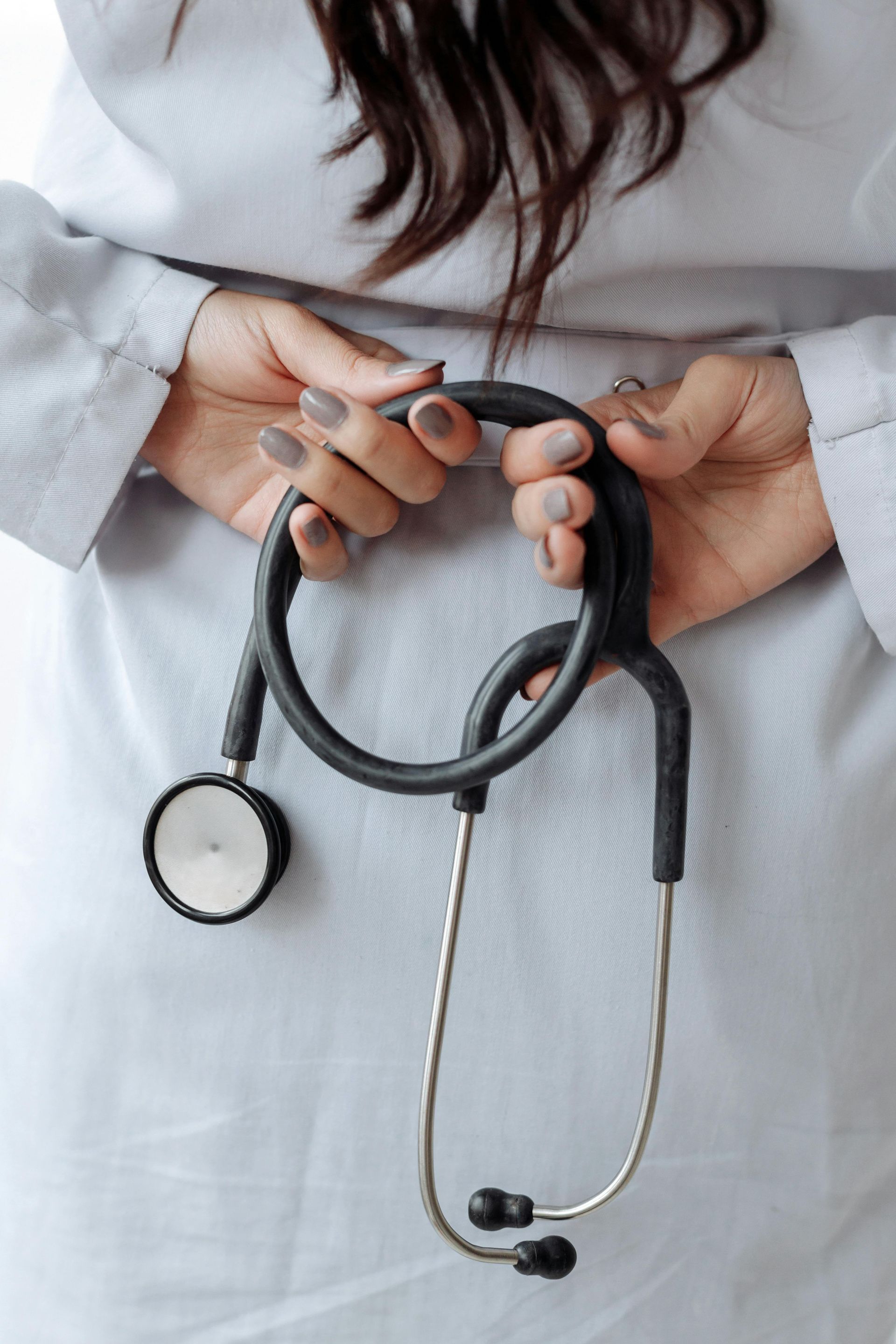 Doctor in white coat holding a stethoscope behind their back.