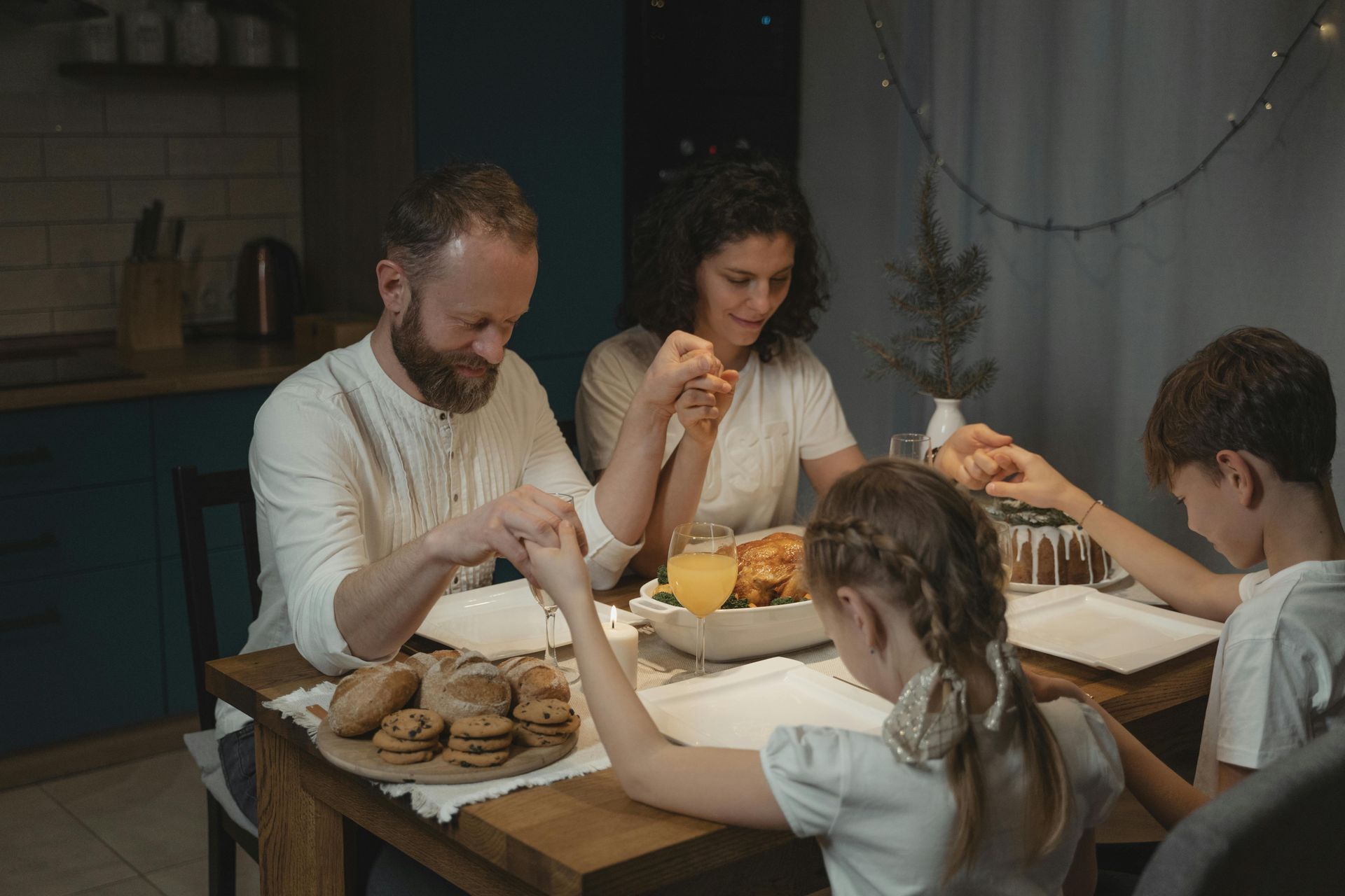 Family holding hands and praying at dinner table.