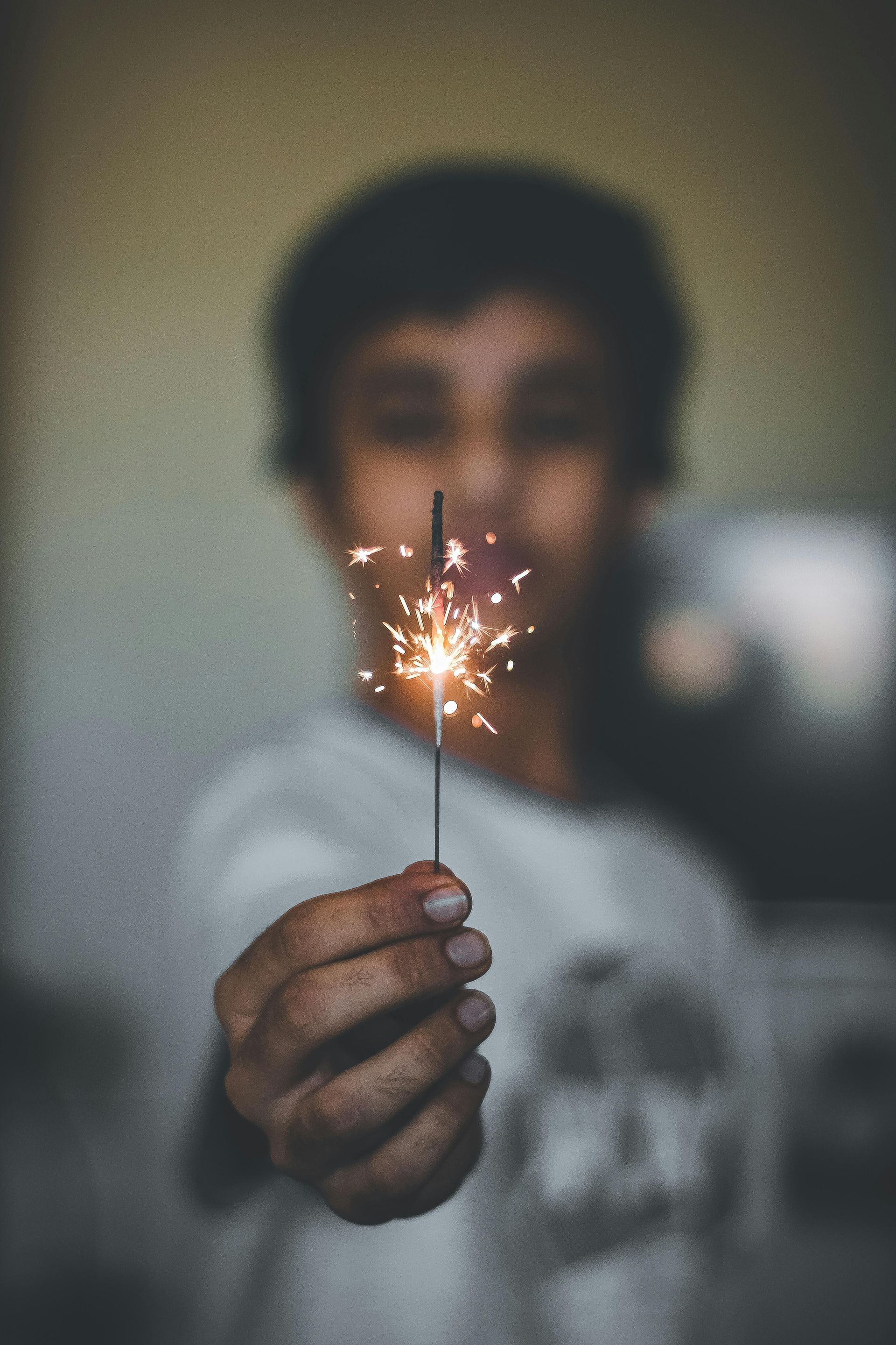 Person holding a lit sparkler, close-up. Sparks radiating, person blurred in the background.